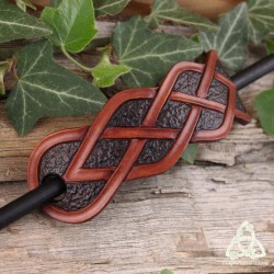 Barrette artisanale en cuir ornée d'entrelacs celtiques infinis marron sur un fond brun foncé texturé.