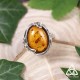 Bague Ellea en argent et Ambre, style Art Nouveau et elfique, vue de face sur fond bois et feuilles, pour cadeau de Noël.